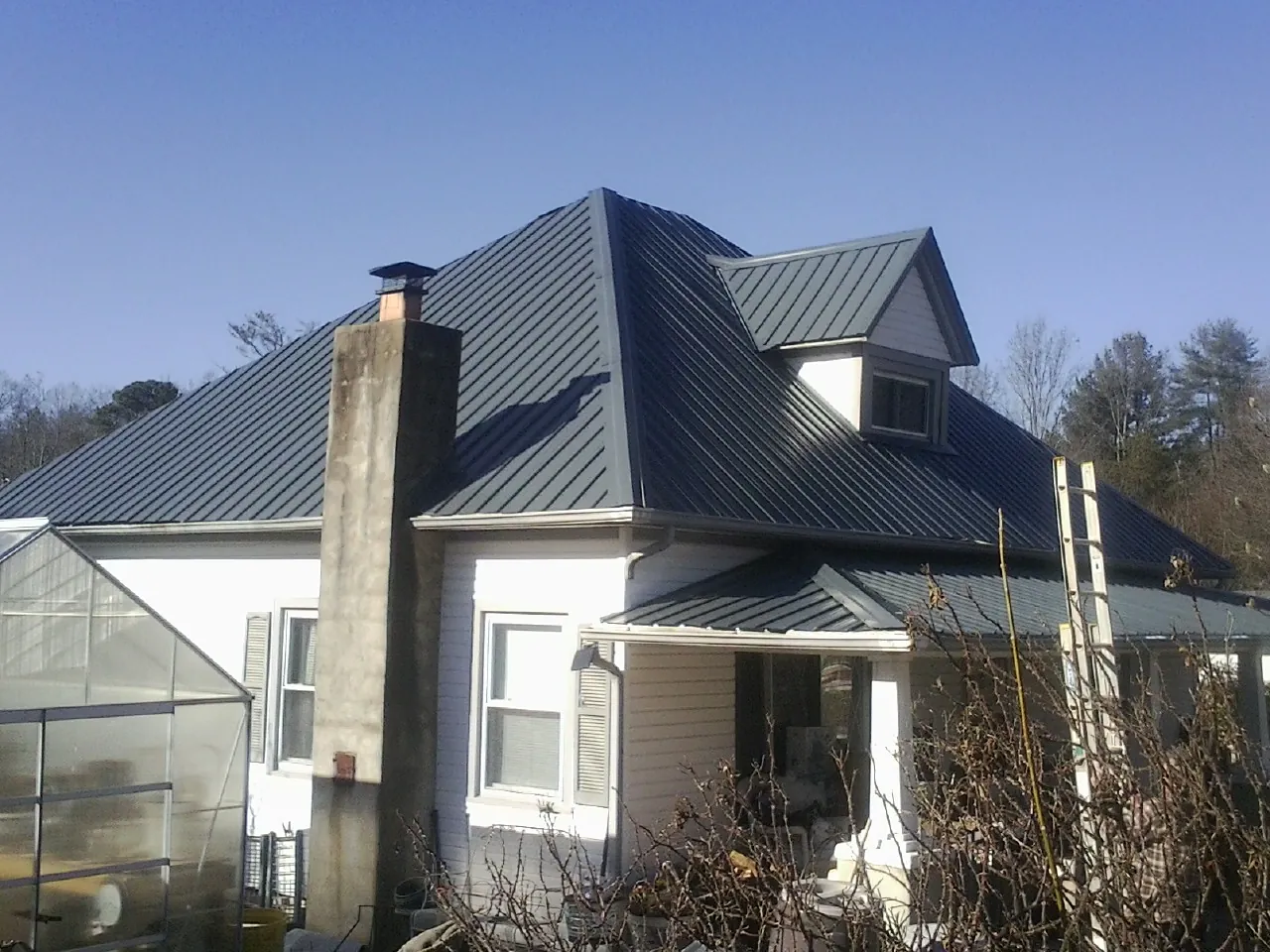 Dark blue standing seam metal roof on a white farmhouse with dormer — Slate & Tile Roof Repair by Roofing Brothers in Prague