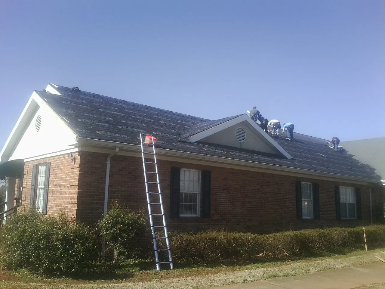 Crew tearing shingles off a brick ranch roof with a ladder set — Emergency Roof Repair work by our crew in Prague