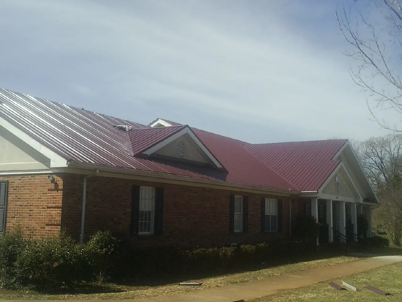 Red metal roof with gabled entries on a long brick building, from a Hail Damage Roof Repair job in Prague