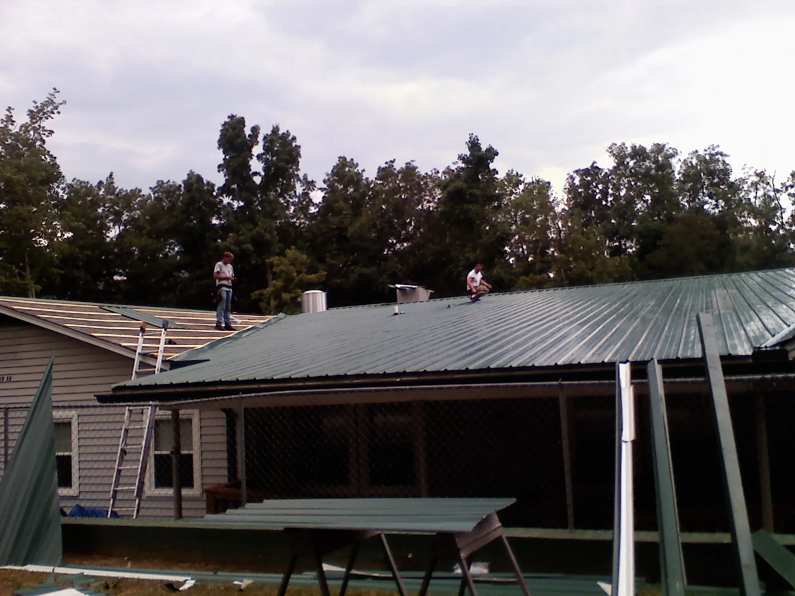 Two roofers installing green metal panels above a covered porch in Prague